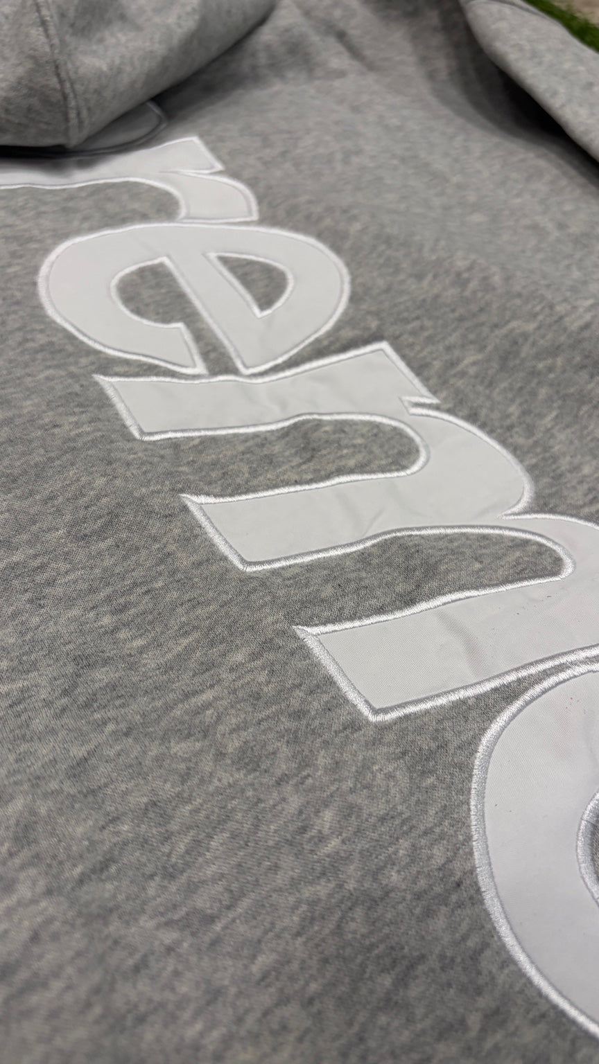 Close-up white raised vertical lettering on back of gray hoodie